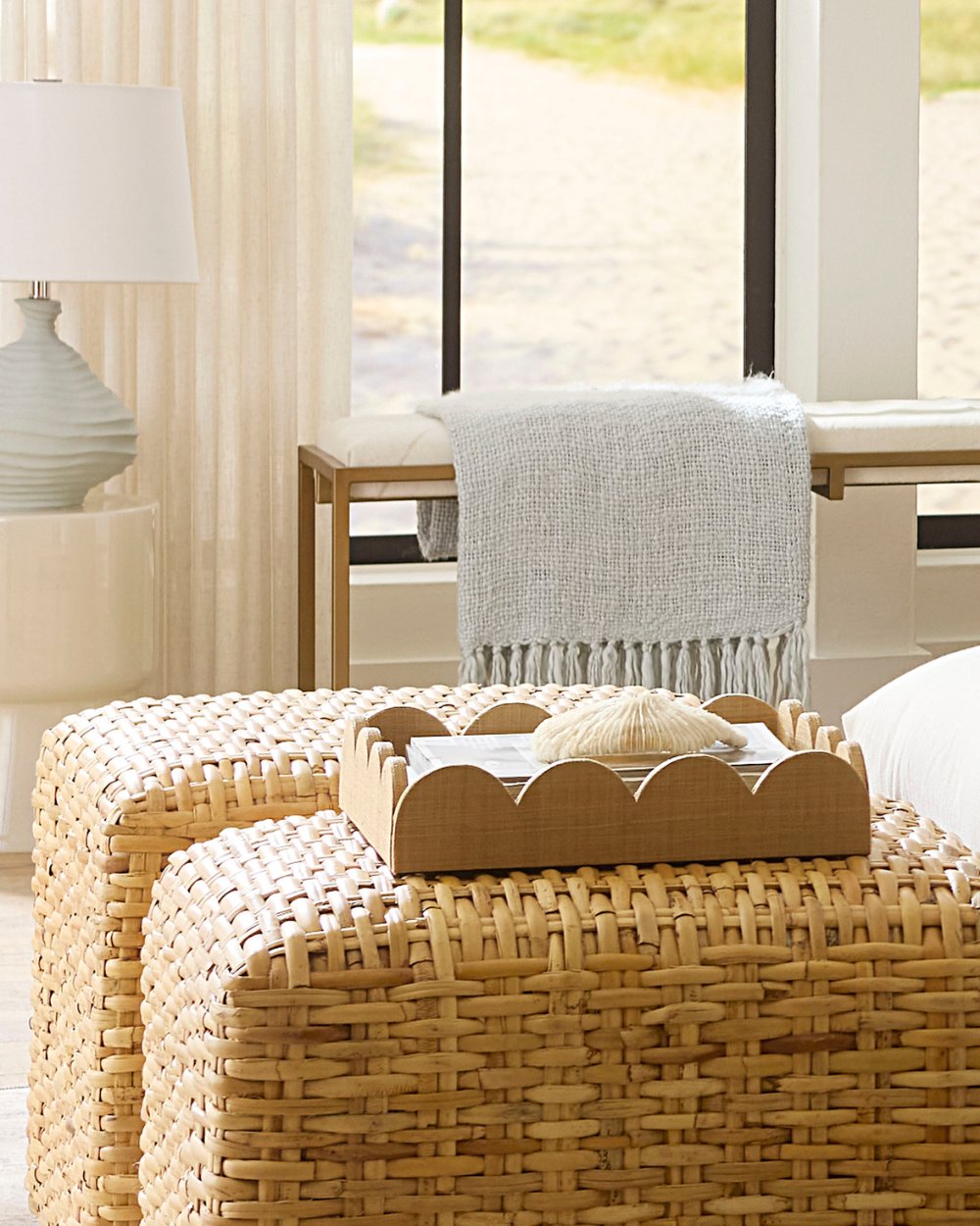 Coastal-inspired interior with woven ottomans, scalloped wood tray, soft blue throw, and a textured ceramic table lamp by Jamie Young; available at Ivory & Olive.