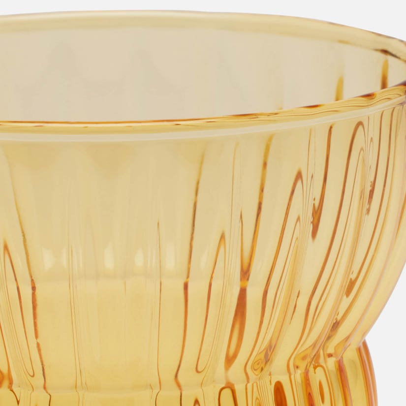 Close-up of a translucent amber glass bowl with vertical ribbed texture and wavy internal lines, shown against a white background.