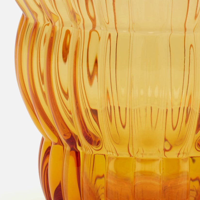Close-up of a translucent amber glass container with a fluted or ribbed surface and warm golden-orange tones against a white background.