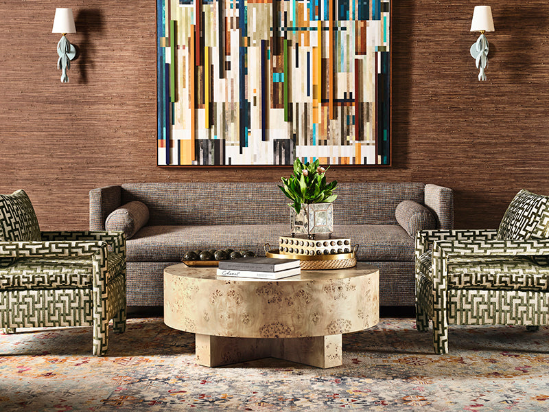 Tinsley sconces flanking a modern abstract artwork in the living room, demonstrating scale. The living room features a gray sofa, patterned armchairs, and a round stone table.