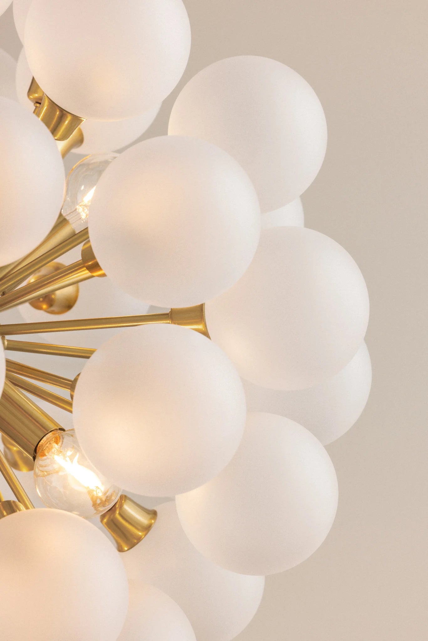 Close-up of a chandelier with gold fixtures and white glass spheres on a neutral background