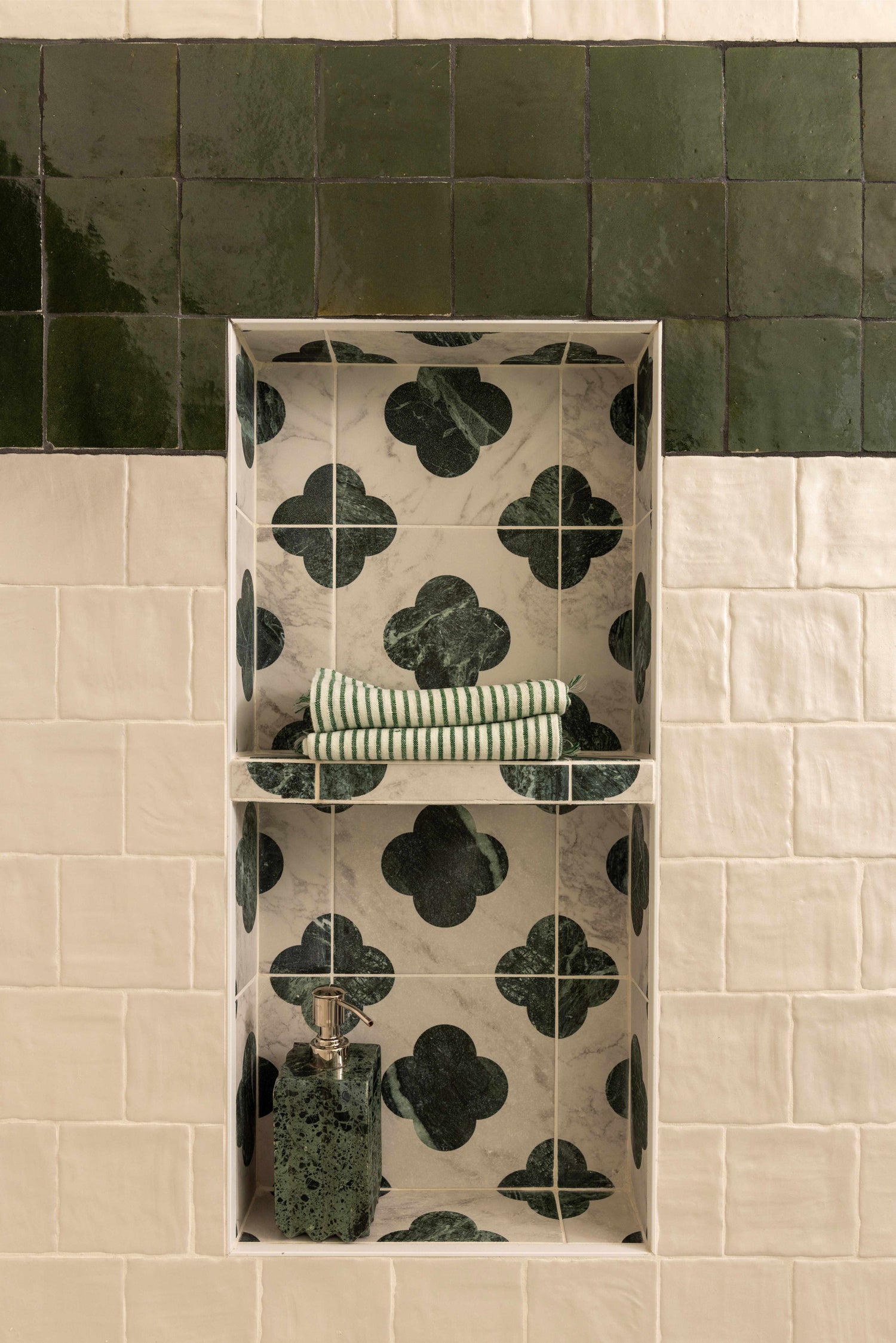Tiled wall with a decorative pattern and a small shelf holding rolled-up towels.