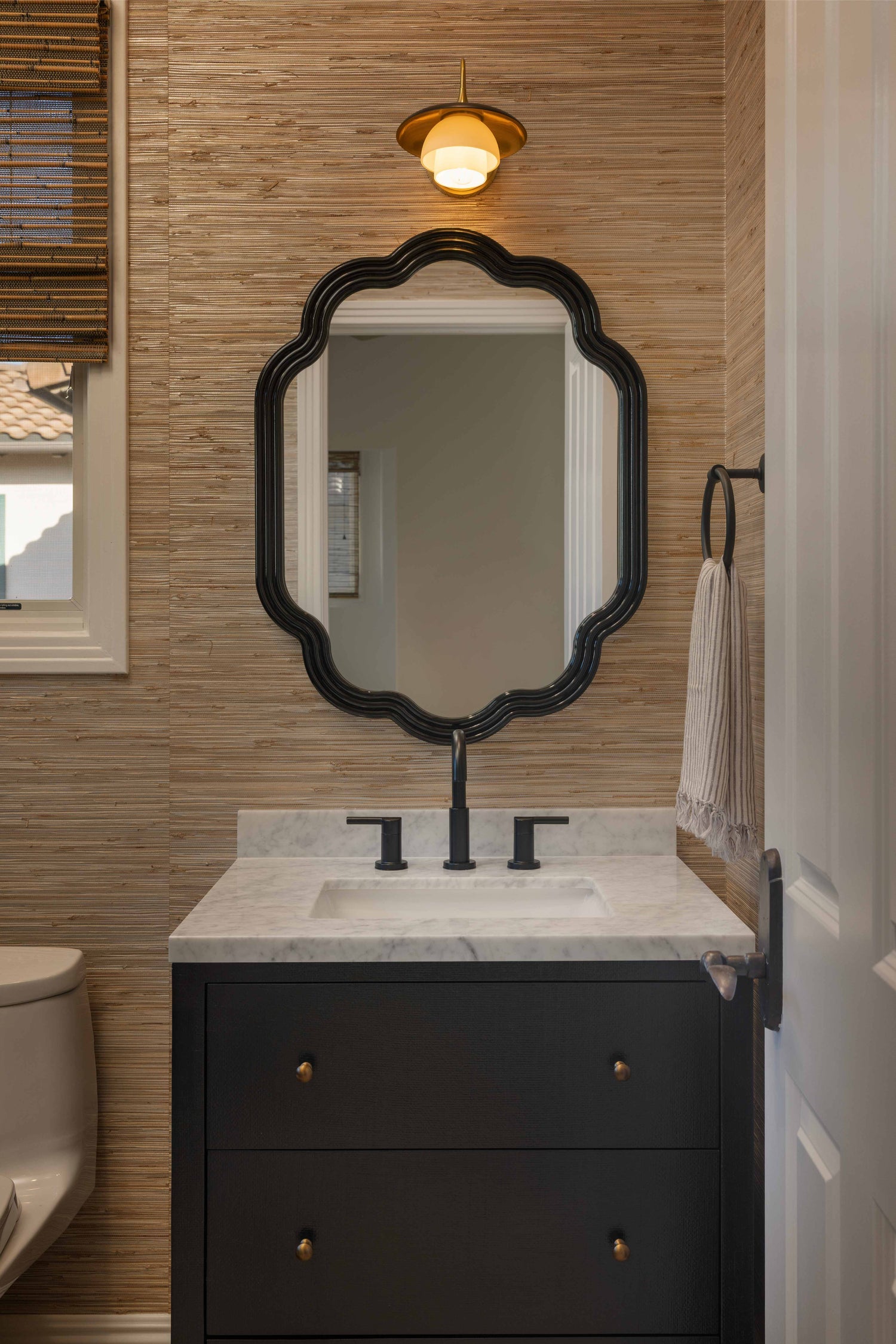 Bathroom with black vanity, marble countertop, and decorative mirror.