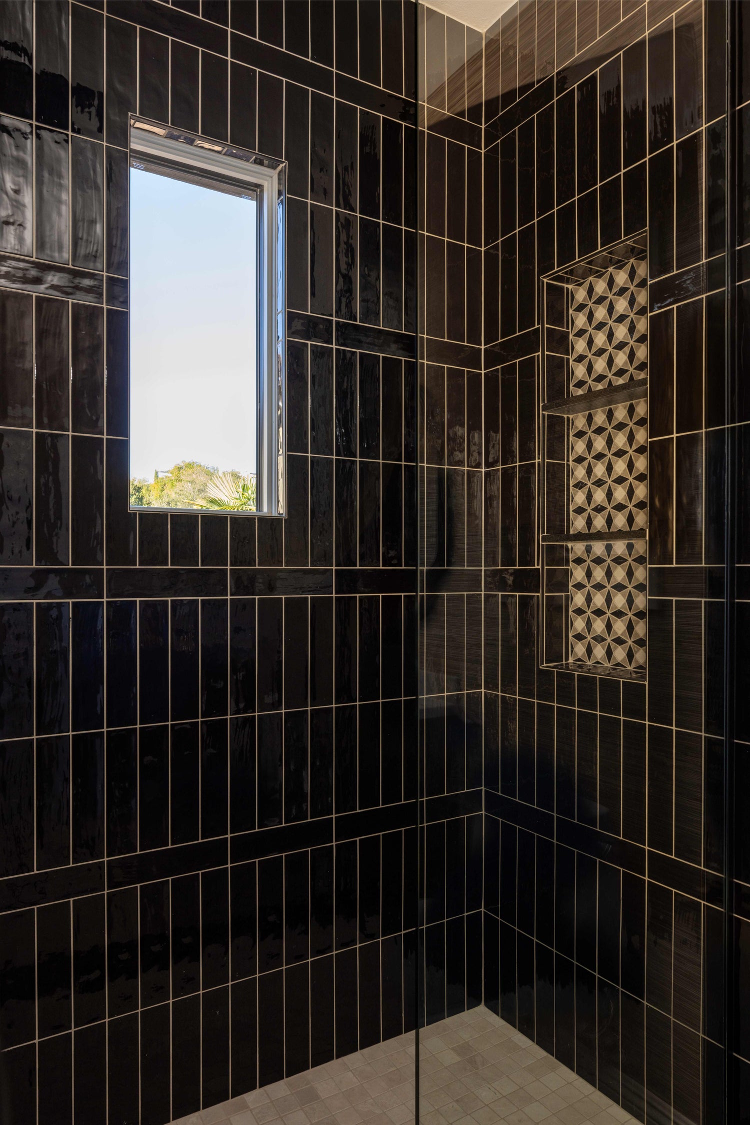Black tiled shower with a window and geometric tile design.