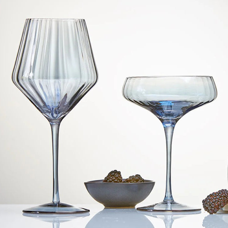 Wine glass and coupe together on a reflective surface with a neutral background