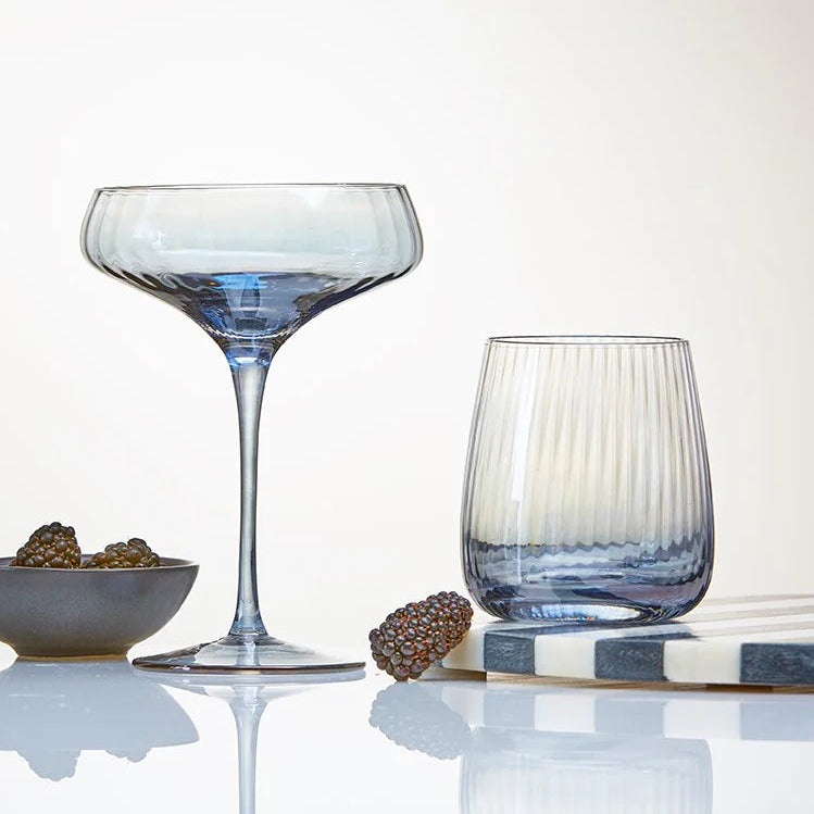 Two wine glasses: coupe and stemless on a reflective surface with a neutral background
