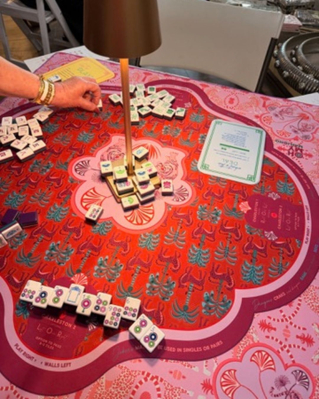 Person playing Mahjong with colorful tiles on a decorative table mat.