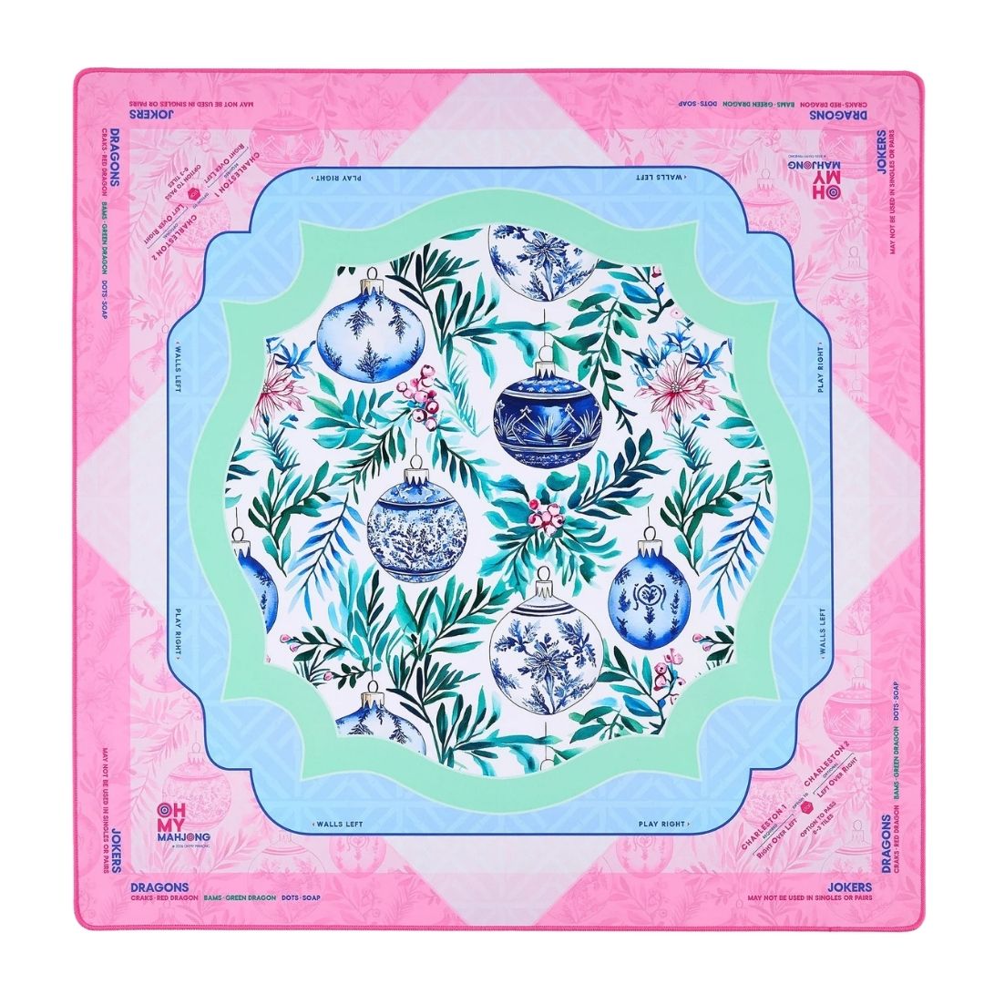 A square Mahjong mat featuring a festive Christmas design with blue and white ornaments, green foliage, and pink accents, framed by a pink border with brand text.