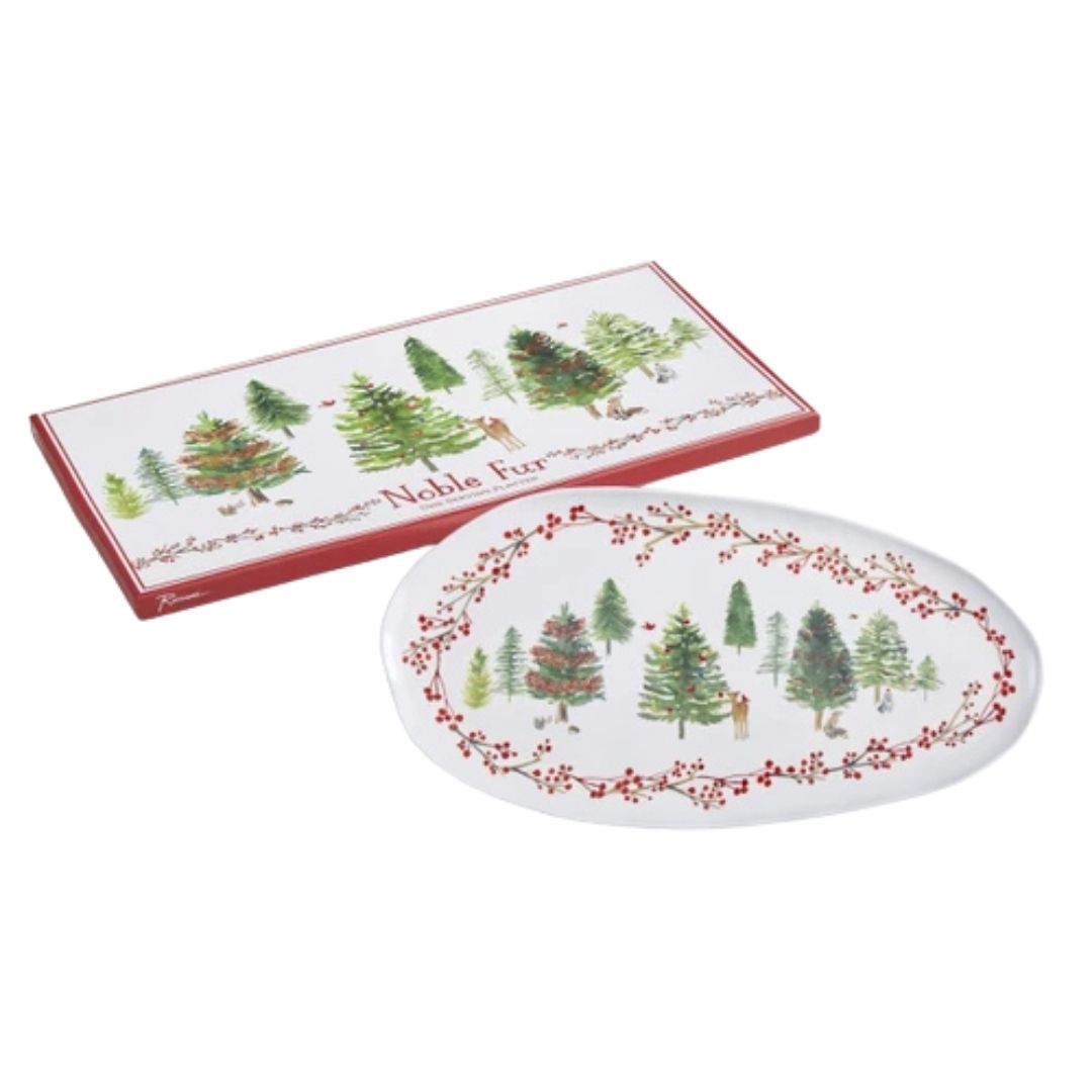 An oval white ceramic plate with a red berry border and a winter forest scene, shown next to its red rectangular gift box featuring matching tree illustrations and the text 'Noble Fur'.