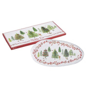 An oval white ceramic plate with a red berry border and a winter forest scene, shown next to its red rectangular gift box featuring matching tree illustrations and the text 'Noble Fur'.