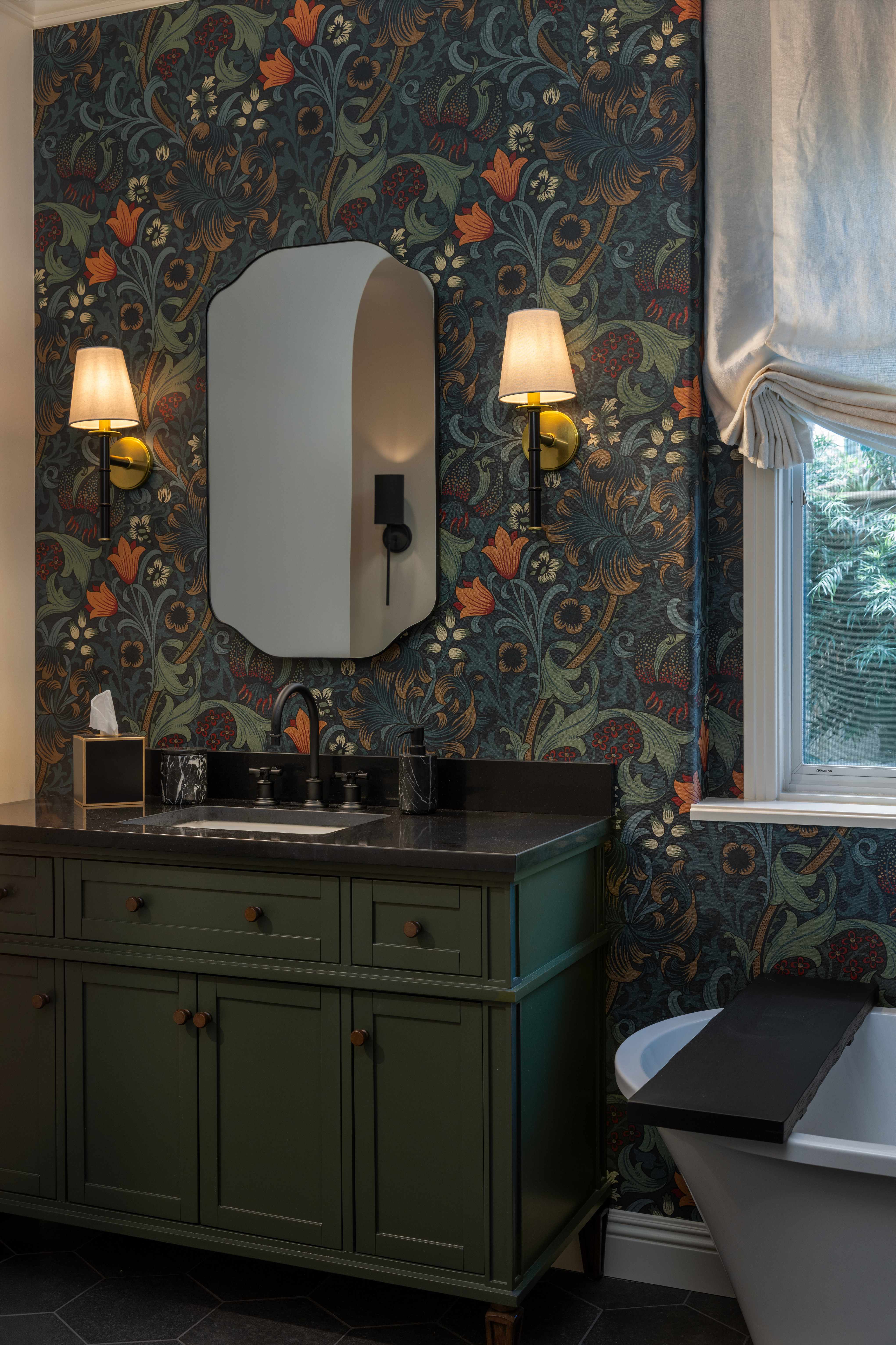 Bathroom with floral wallpaper, green vanity, and white bathtub.