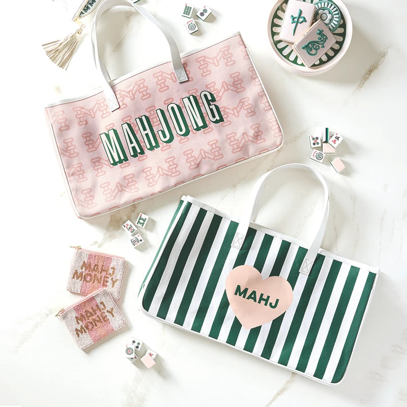 Two mahjong bags, one pink with 'MAHJONG' text and the other green and white striped, surrounded by mahjong pieces on a light background.