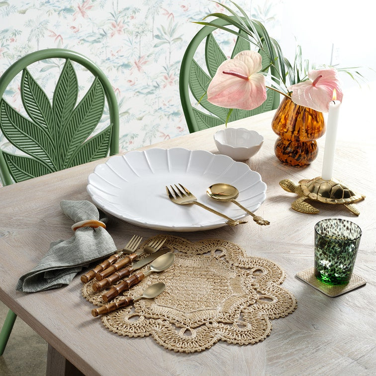 Dining table setting with white plates, gold cutlery, and decorative items on a light wooden table.