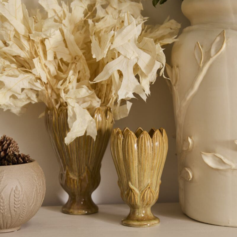 Decorative ceramic vases on a white shelf, including a tall ribbed vase with dried cream leaves, a smaller matching ribbed vase, and a large cream embossed ceramic planter.